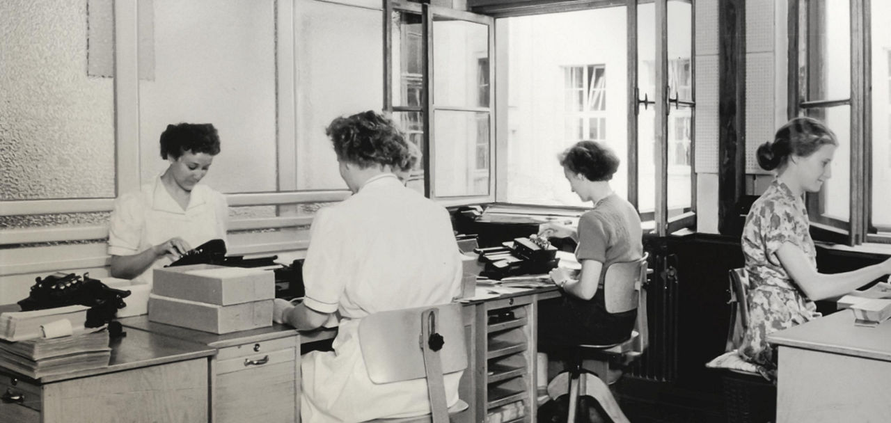 Es handelt sich um ein historisches Bild, das vier Frauen bei der Arbeit in der Sparda-Bank Hannover zeigt.