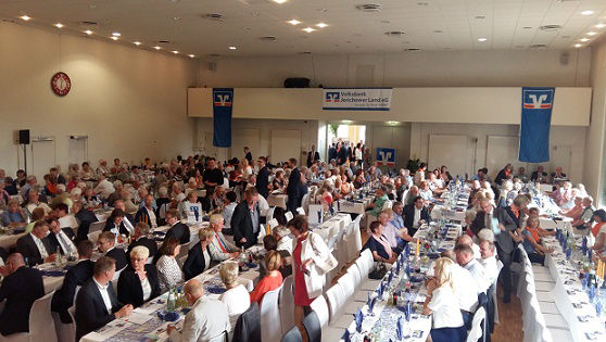 Ein großer Bankettsaal ist mit Menschen gefüllt, die an langen Tischen sitzen und eine Mahlzeit genießen.