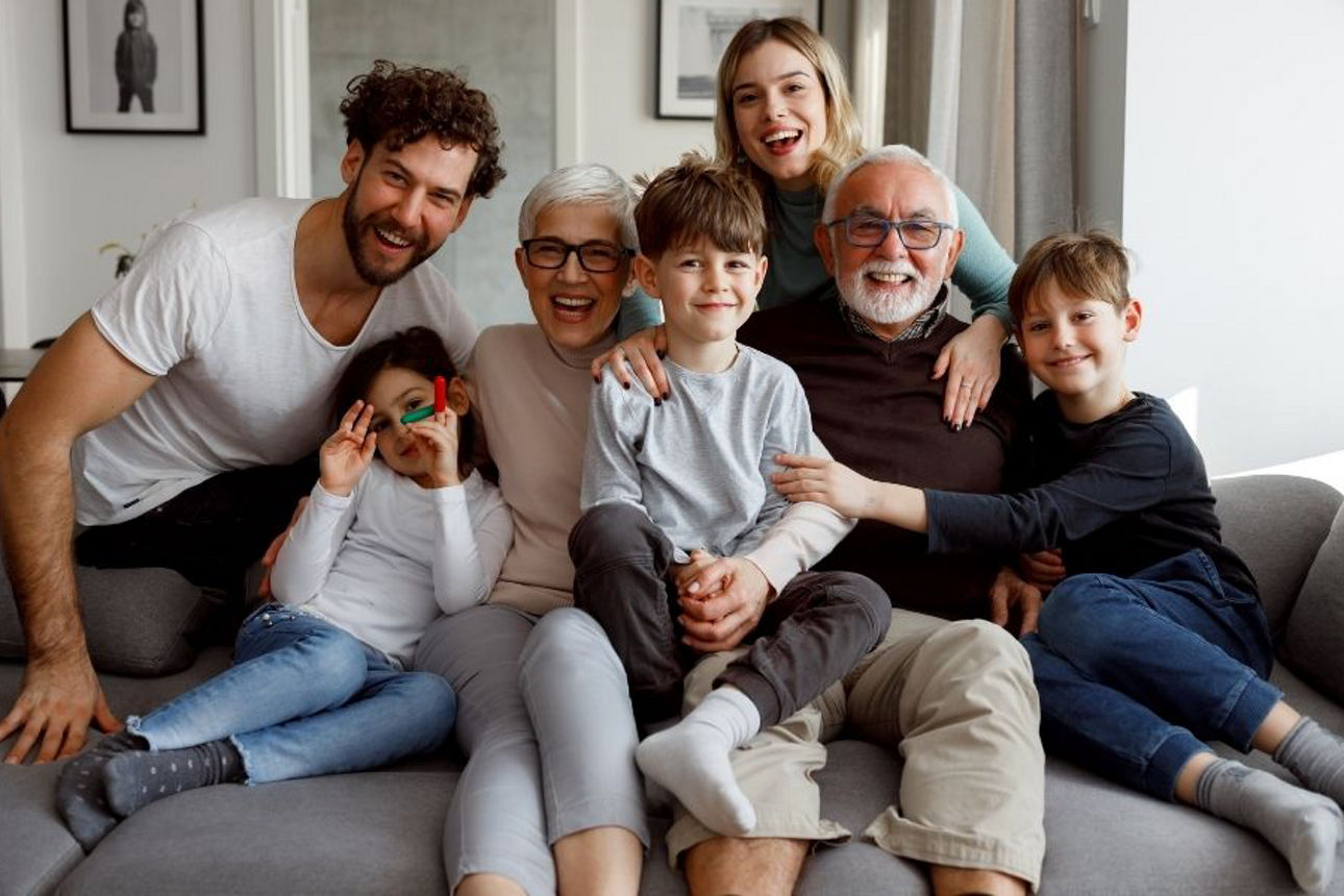 7 Familienmitglieder aus 3 Generationen sitzen freudestrahlend auf der Couch