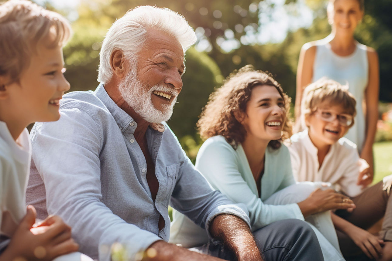 Ein alter Mann mit seiner Familie sitzt lachend auf einer Wiese