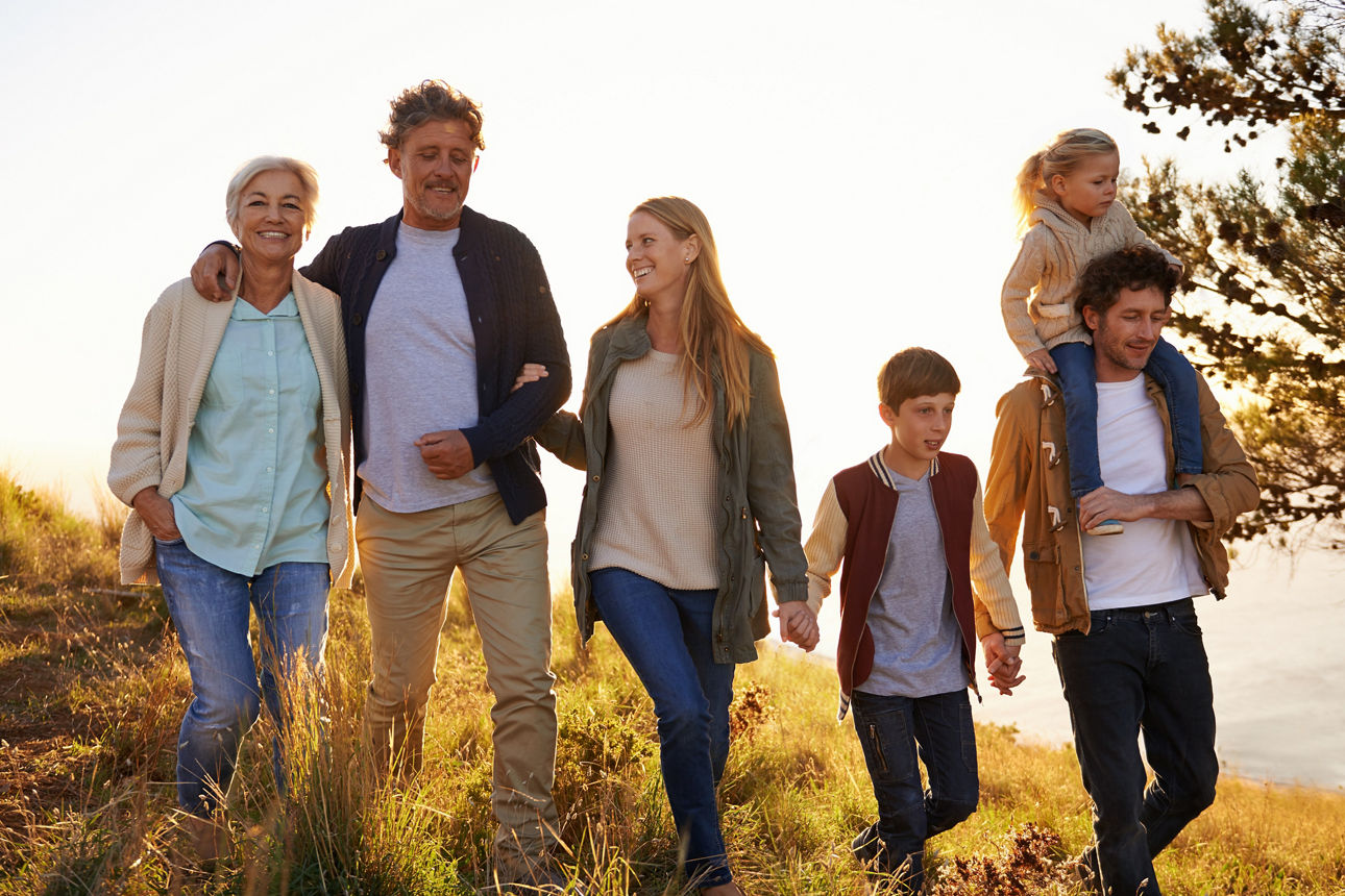 Familie aus mehreren Generationen laufen händchenhaltend auf einer Wiese im Herbst