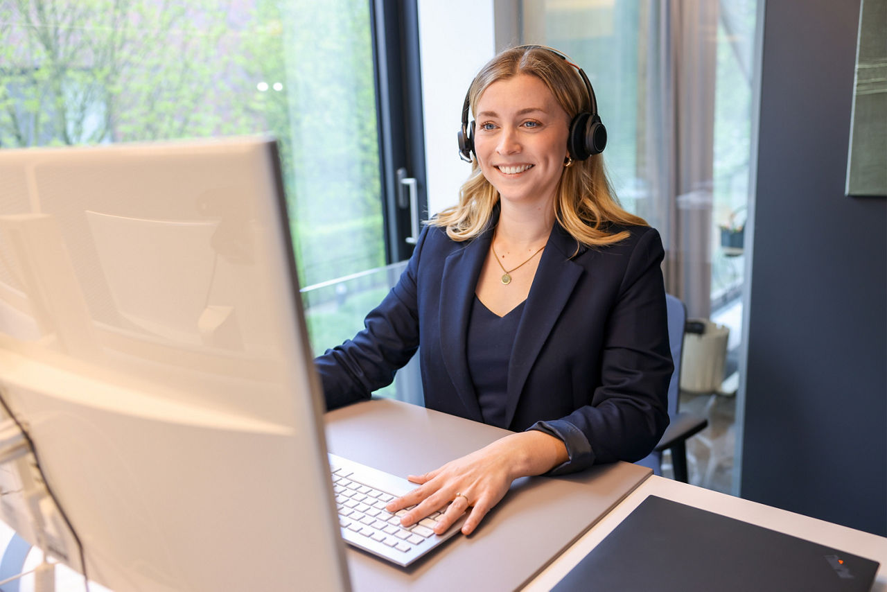 Lisa Marie Beckmann steht an einem Schreibtisch und nimmt mit Headset an einem Meeting teil