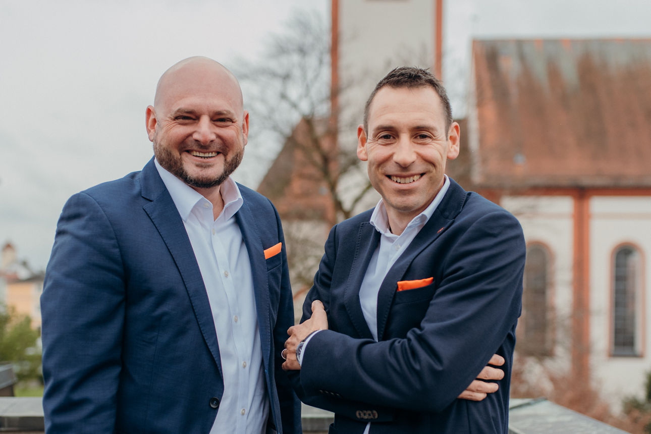 Zwei Männer lachend vor verschwommenen Kirche im Hintergrund