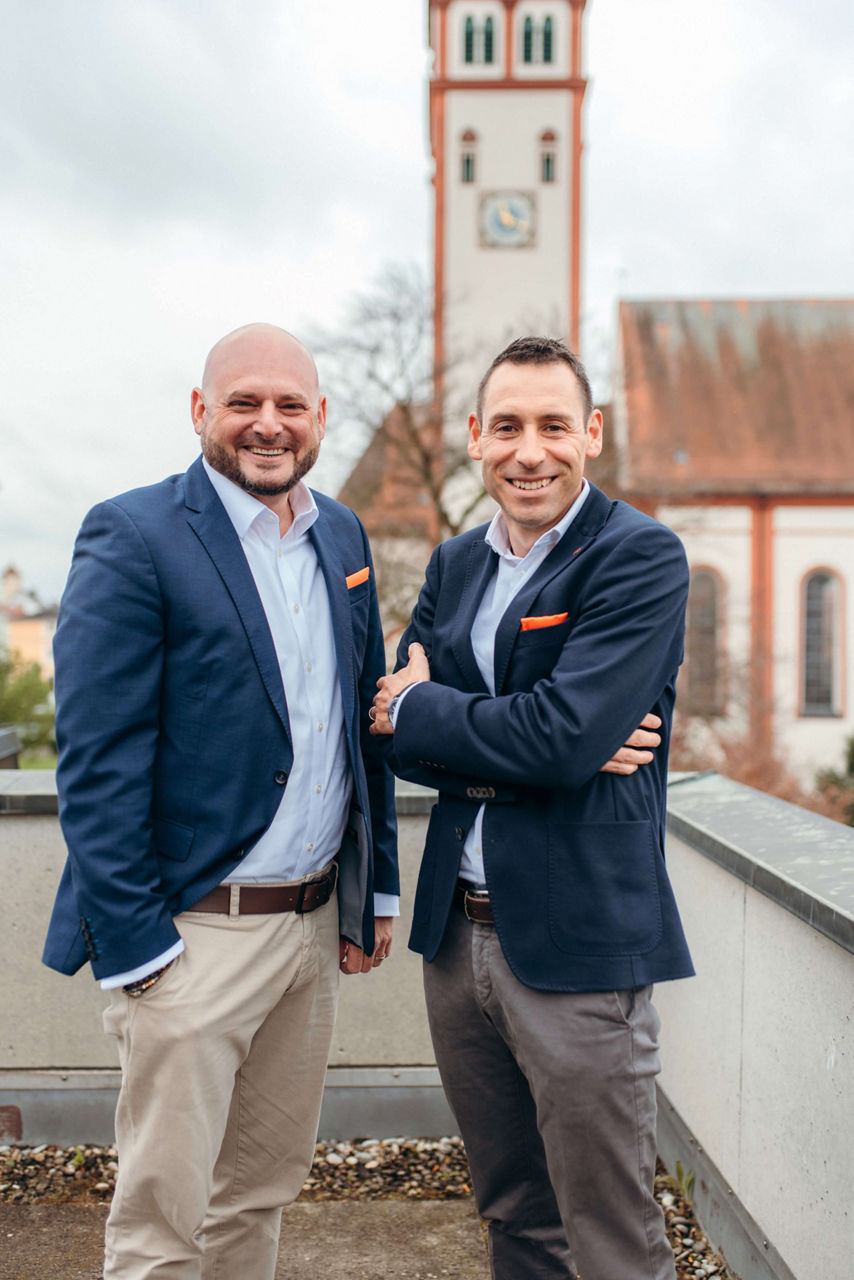 Zwei Männer lachend vor verschwommenen Kirche im Hintergrund