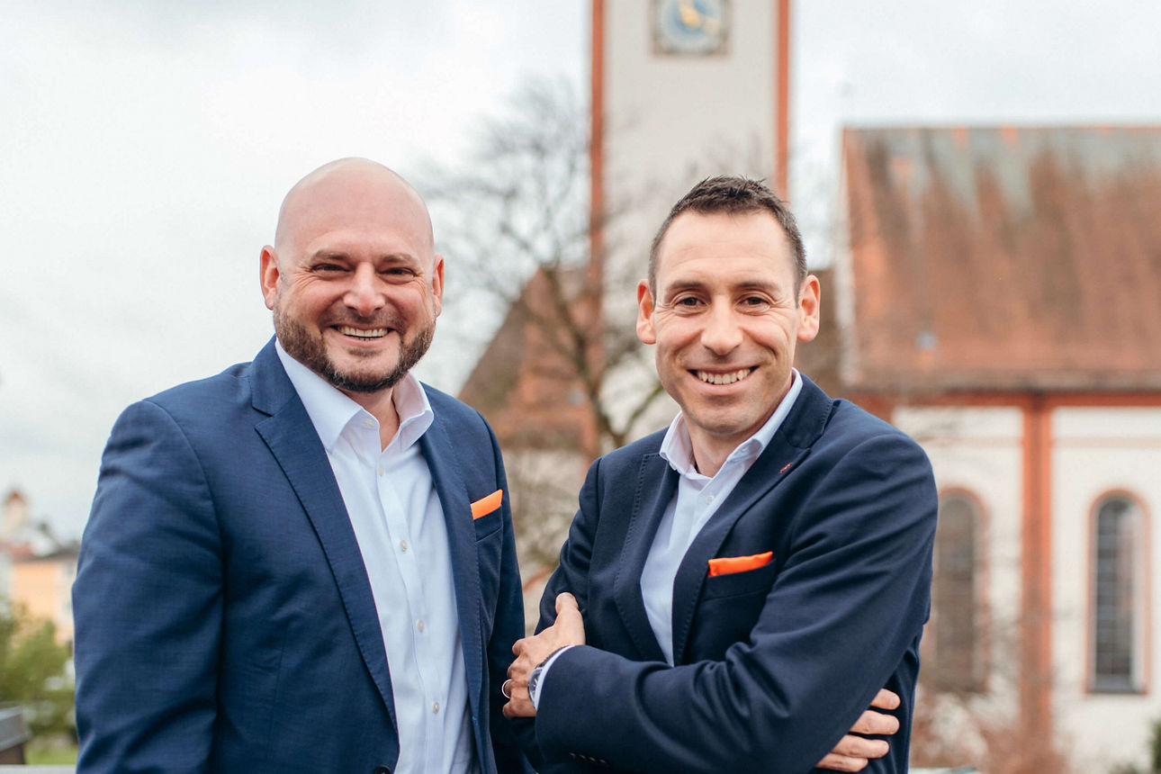 Zwei Männer lachend vor verschwommenen Kirche im Hintergrund