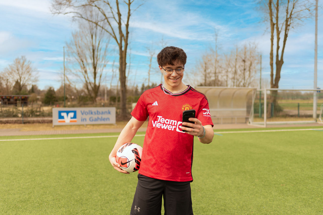 Junger Mann mit Handy und Fußball in der Hand
