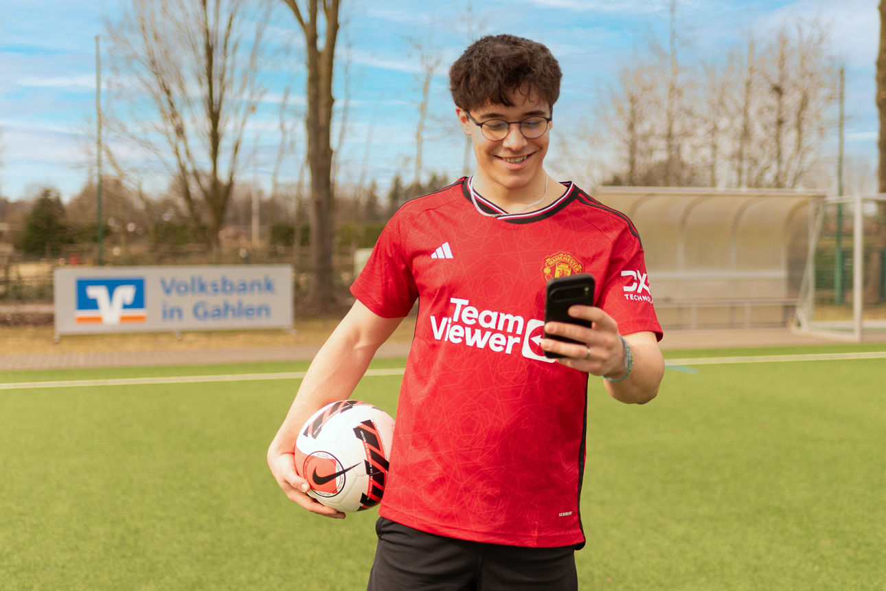 Junger Mann mit Handy und Fußball in der Hand