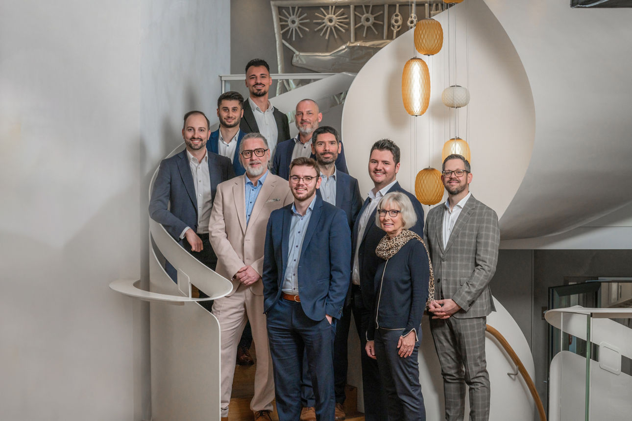 eine Frau und mehrere Männer im Casual Business Outfit stehend auf einer weißen Wendeltreppe