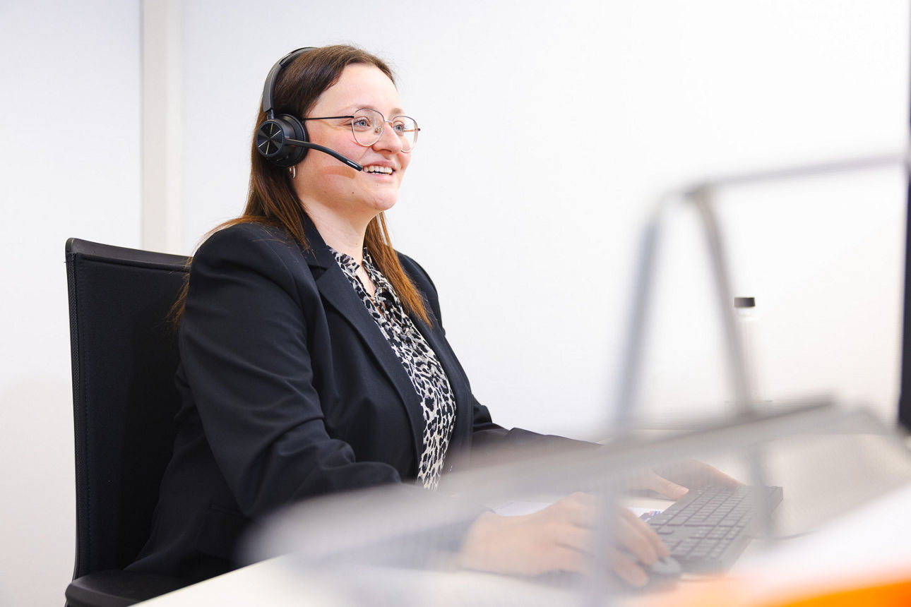 Frau mit Headset sitzt am Schreibtisch