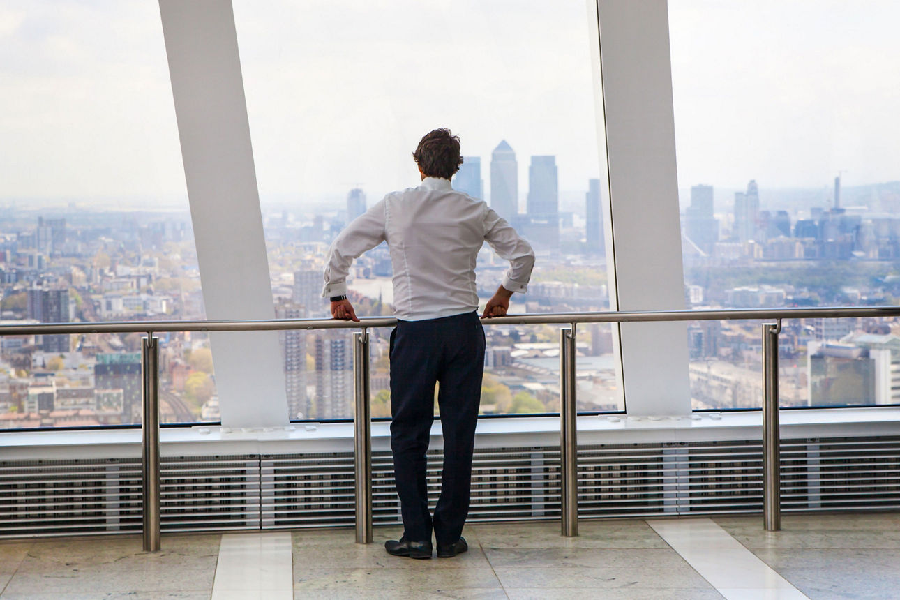 Geschäftsmann, der London durch das Fenster des Walkie Talkie-Gebäudes betrachtet. Die Ansicht umfasst die Geschäfts- und Bankingareale von Canary Wharf.