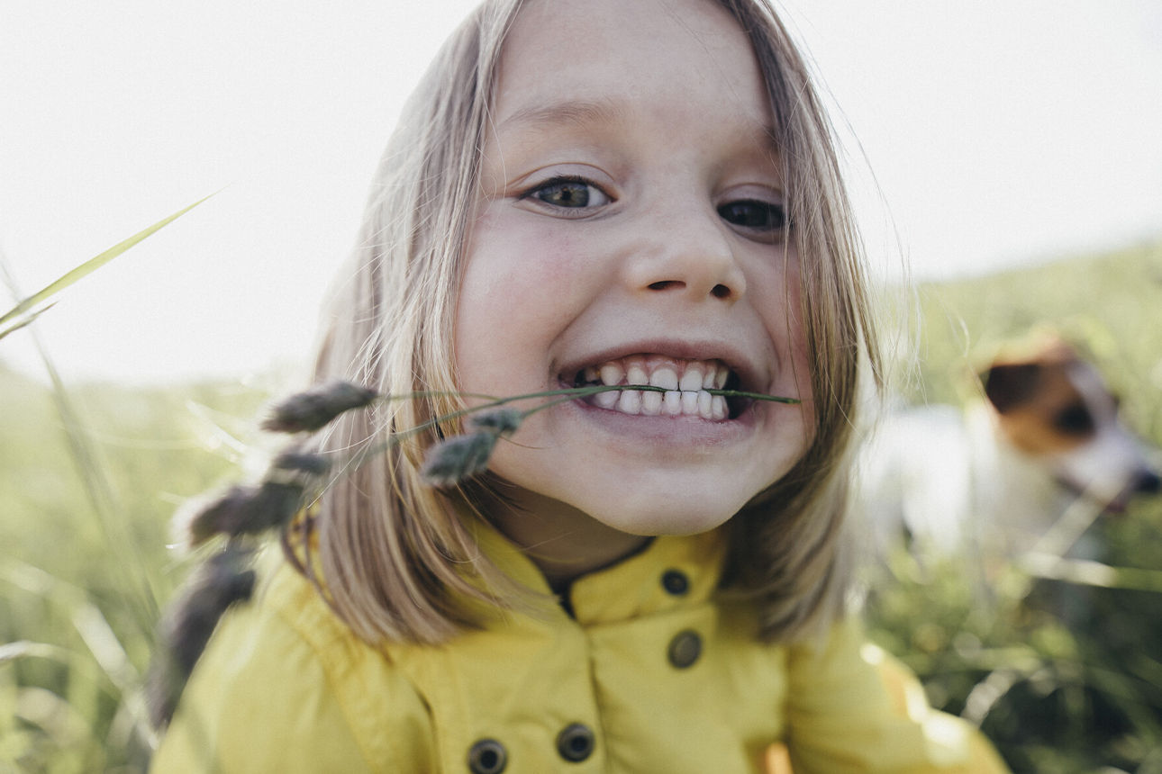 Kleinkind auf einer Wiese mit einen Haferstrauch im Mund 