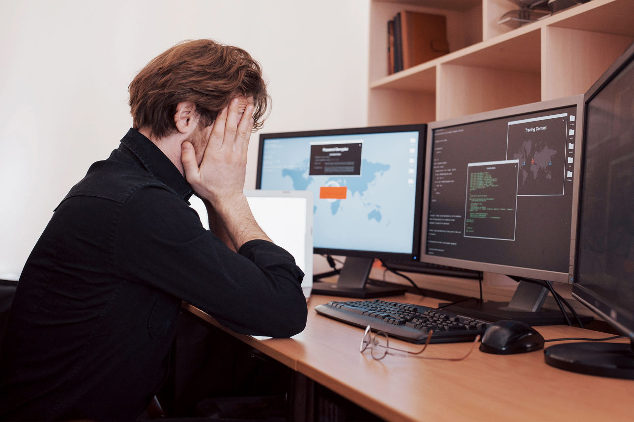 The young dangerous hacker breaks down government services by downloading sensitive data and activating viruses. A man uses a laptop computer with many monitors.
