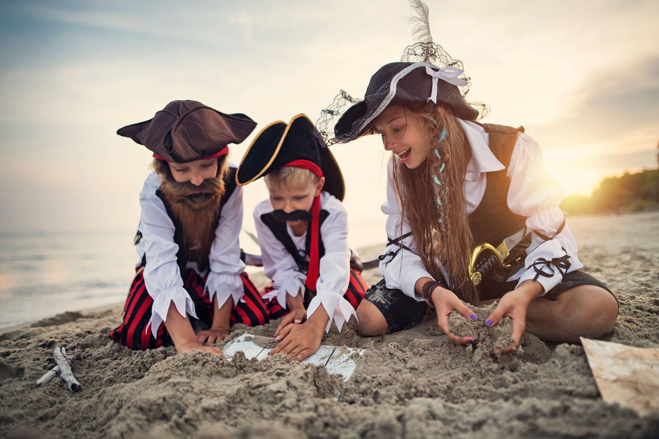 Three little pirates, a girl and two boys are playing pirates on the beach. They have found a treasure chest buried in the beach sand.Sunny summer day.Nikon D850