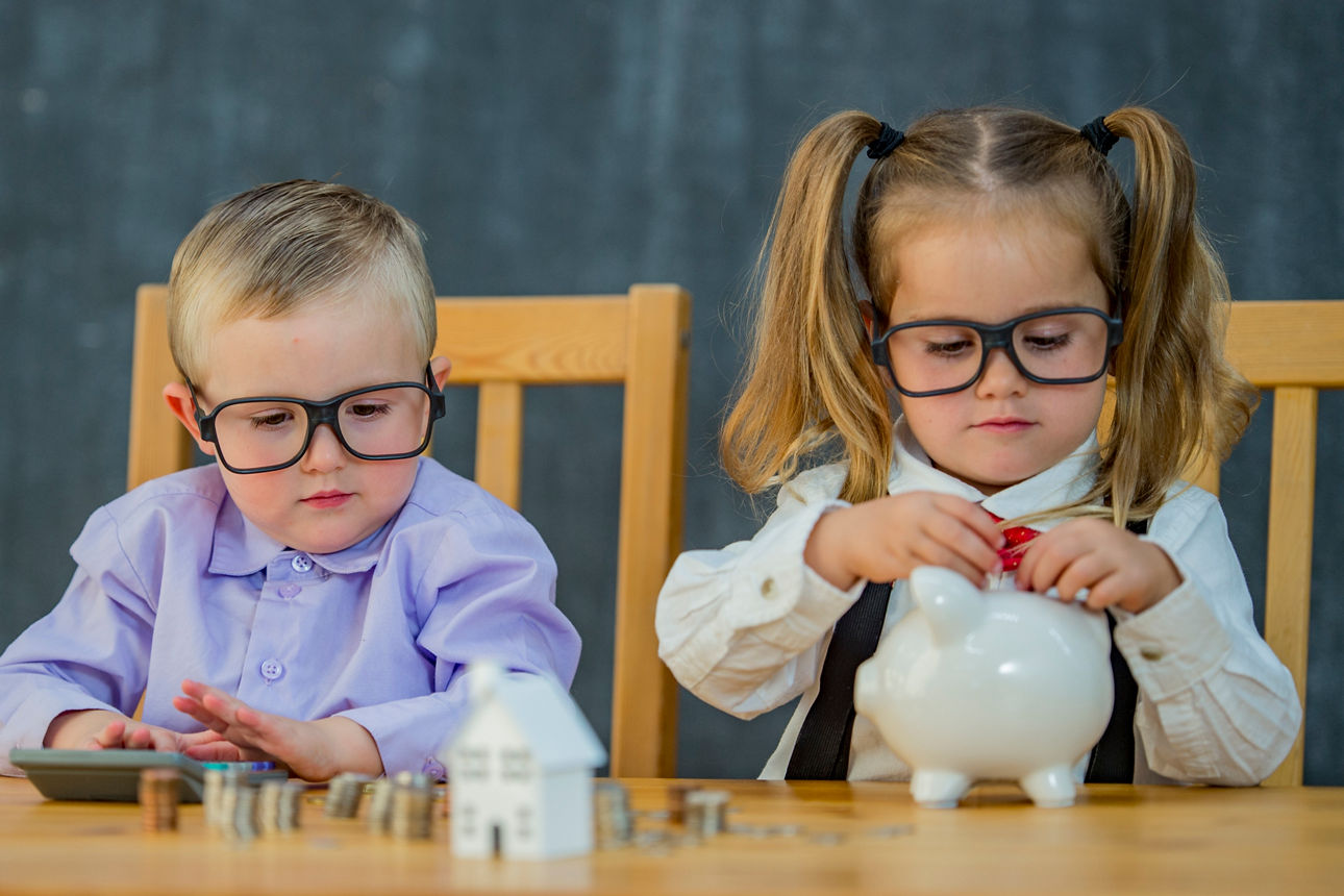 Zwei Kinder sitzen am Tisch und zählen gemeinsam mit ihren Spardosen ihr Geld