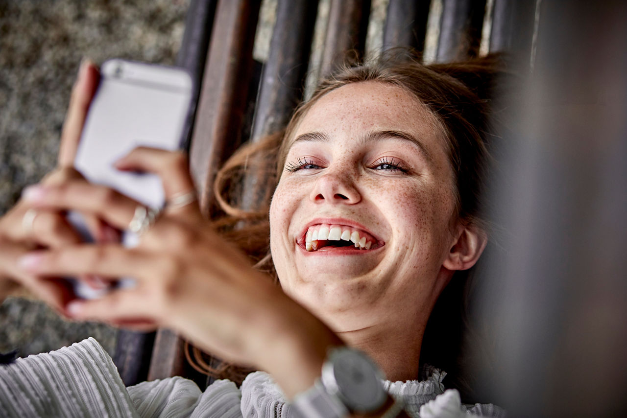 Junge Frau hält ihr Handy und lächelt 