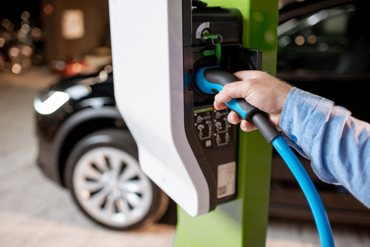 Man plugging cable into the charging station for electric cars at the car dealership, close-up view