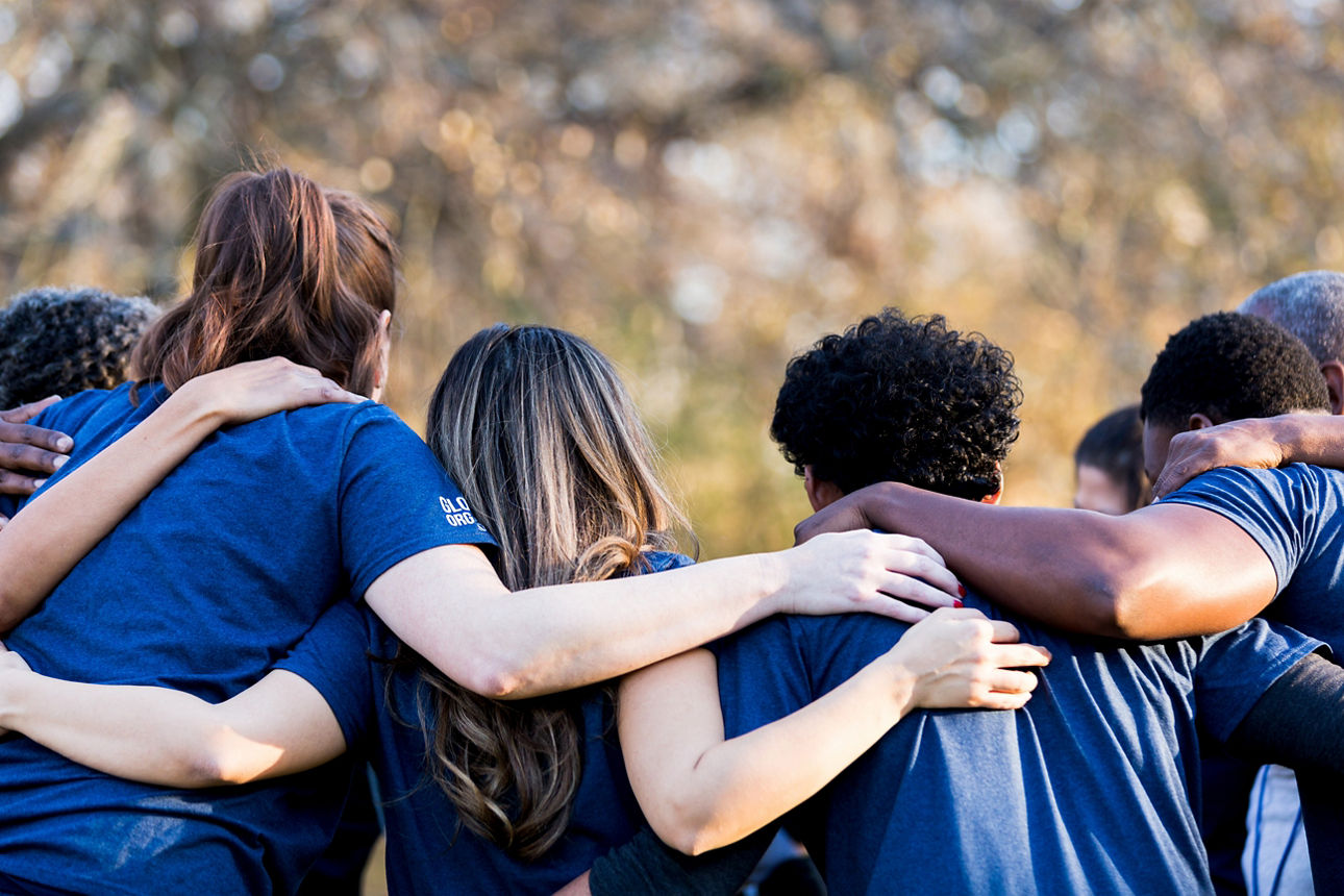 Diverse group of friends cleanup a park during a charity event. They are standing with their arms around one another.