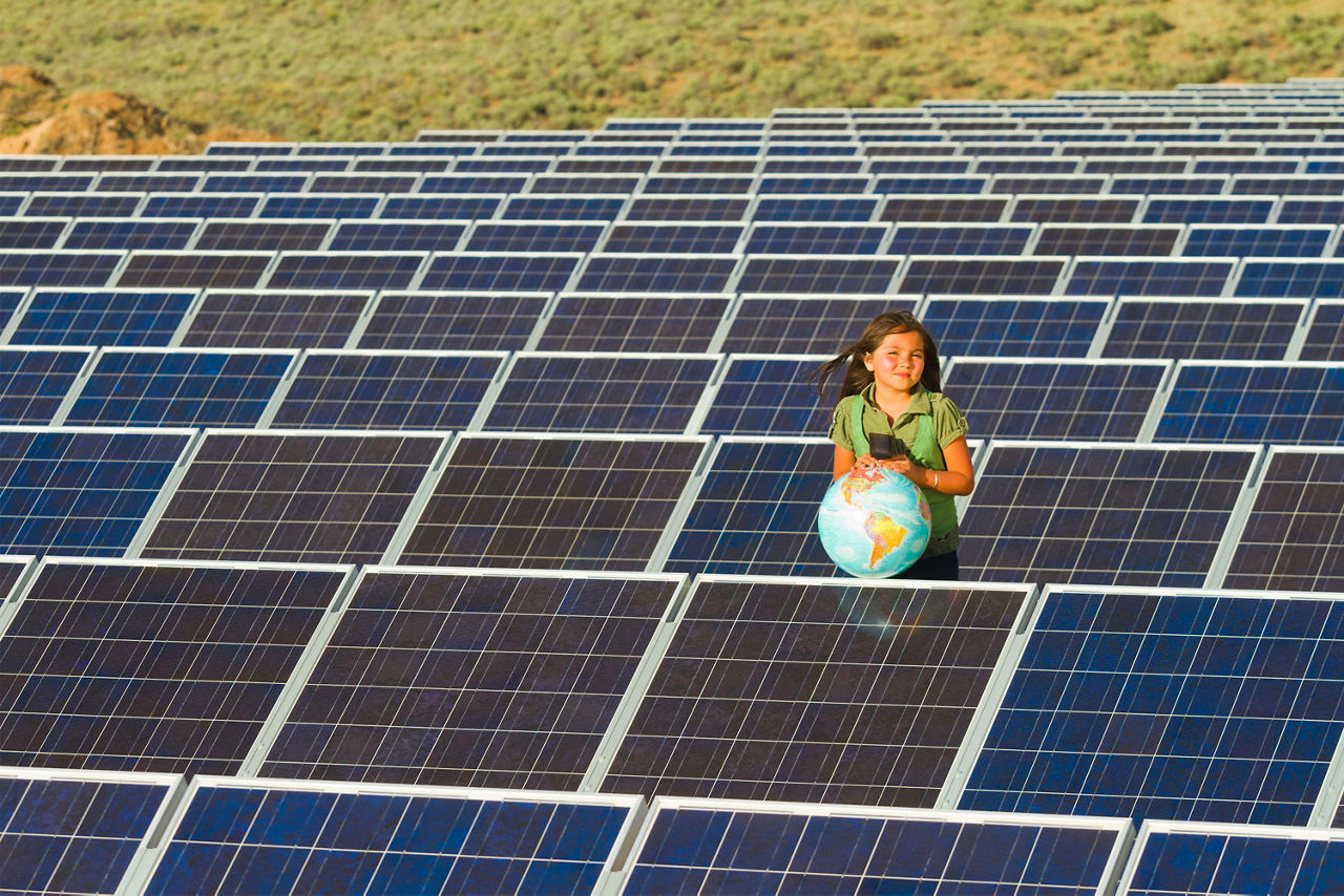 Ein Mädchen hält eine Weltkugel in den Händen und steht vor einer Solaranlage