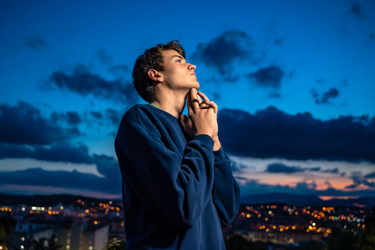 Junger Mann steht nachdenklich im Freien vor blauem Himmel