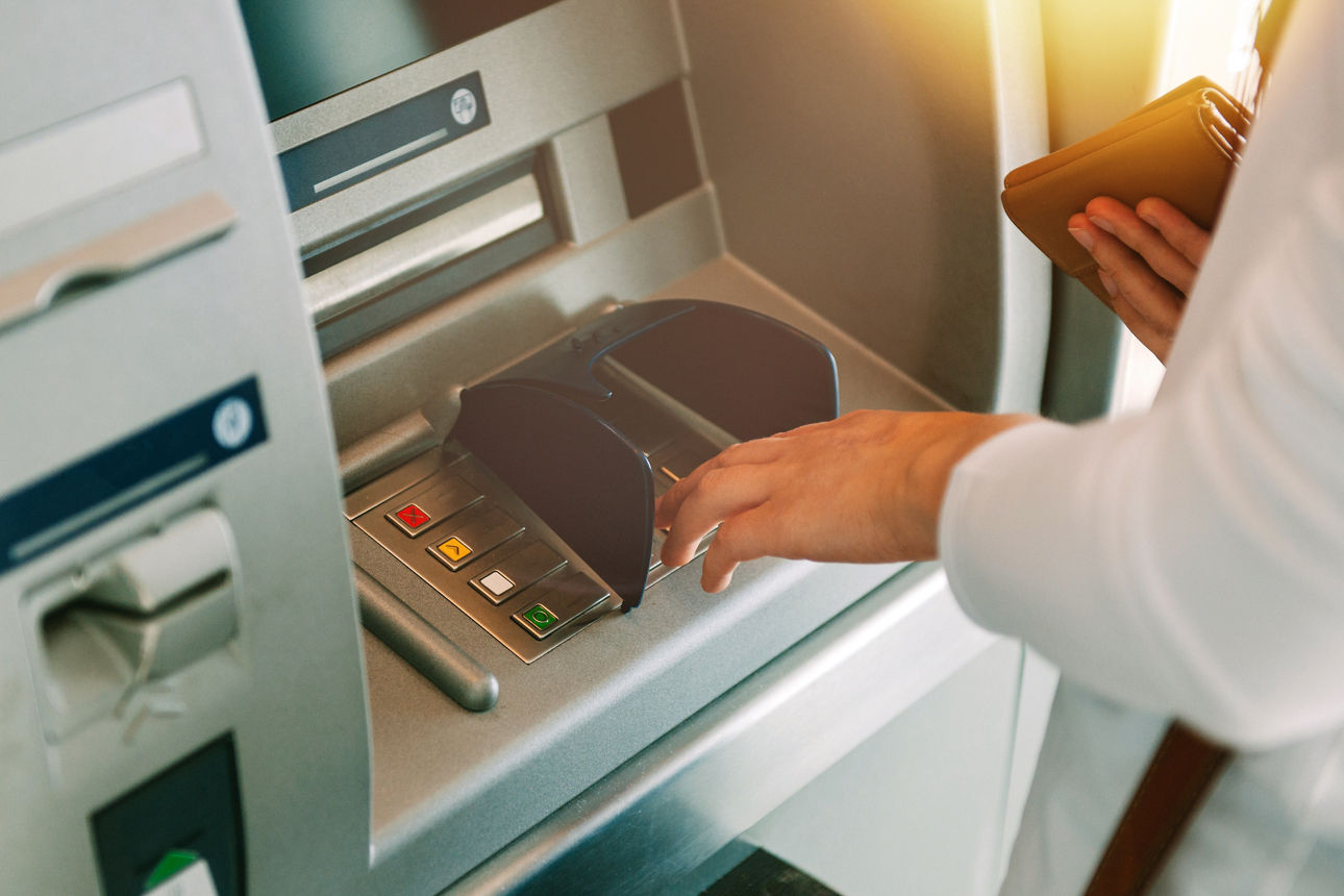 Woman using ATM holding wallet an pressing the PIN security number on the keyboard automatic teller machine