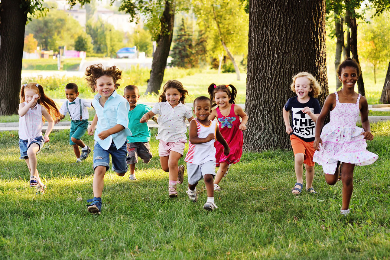 A group of happy children of boys and girls run in the Park on the grass on a Sunny summer day . The concept of ethnic friendship, peace, kindness, childhood.