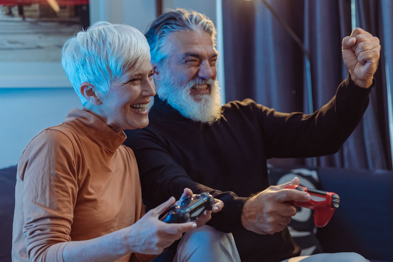 Fröhliches älteres Ehepaar, das Gaming-Controller in den Händen hält, Videospiele spielt und Spaß hat.