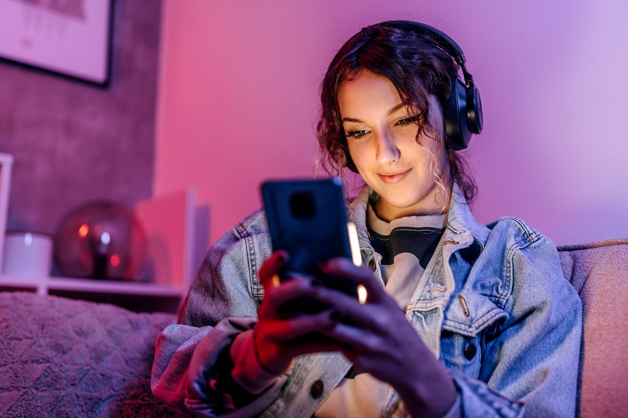 Junge Frau benutzt ihr Smartphone, während sie nachts zu Hause auf dem Sofa sitzt