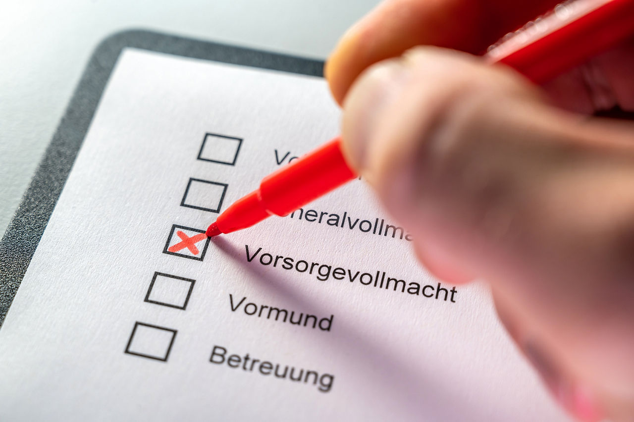 Getty1466908169-Liste mit Punkten zur Vorsorge und Hand mit rotem Filzstift, die Kreuz bei Vorsorgevollmacht macht
