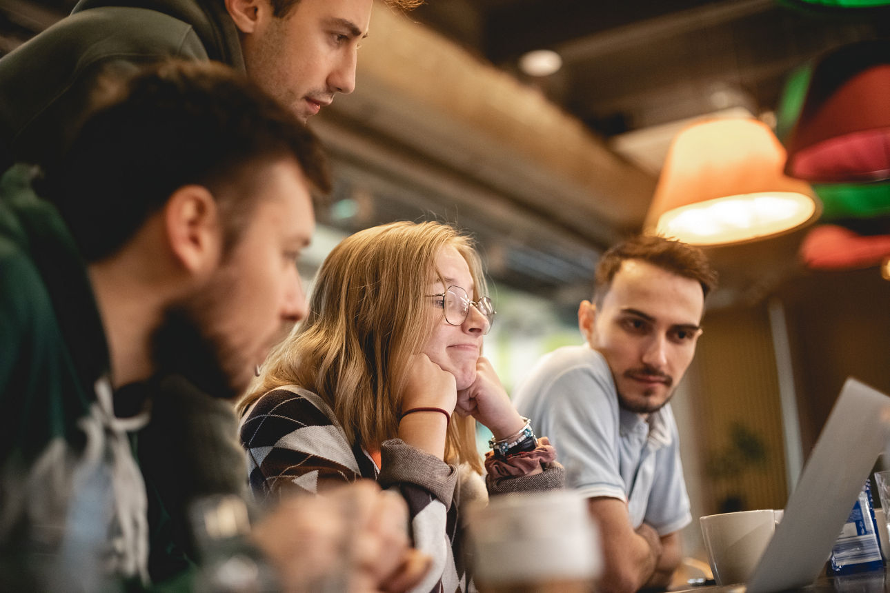 Group portrait of young people indoors who working with laptop. People wear casual clothing. Close-up photography, blurred background. Woman and men on the meeting in coworking modern office