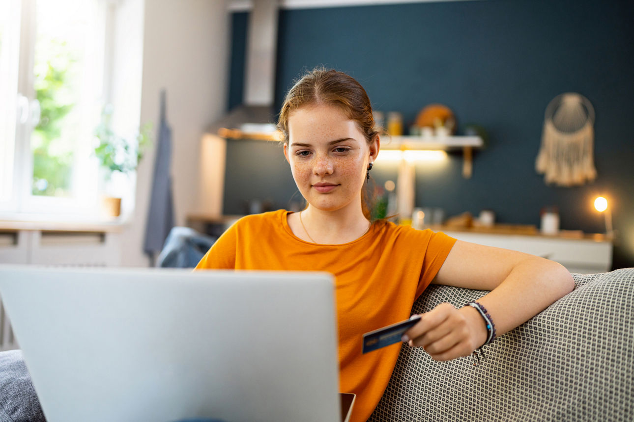 Junges Mädchen auf dem Sofa sitzt mit einer Kreditkarte in der Hand vor einem Laptop