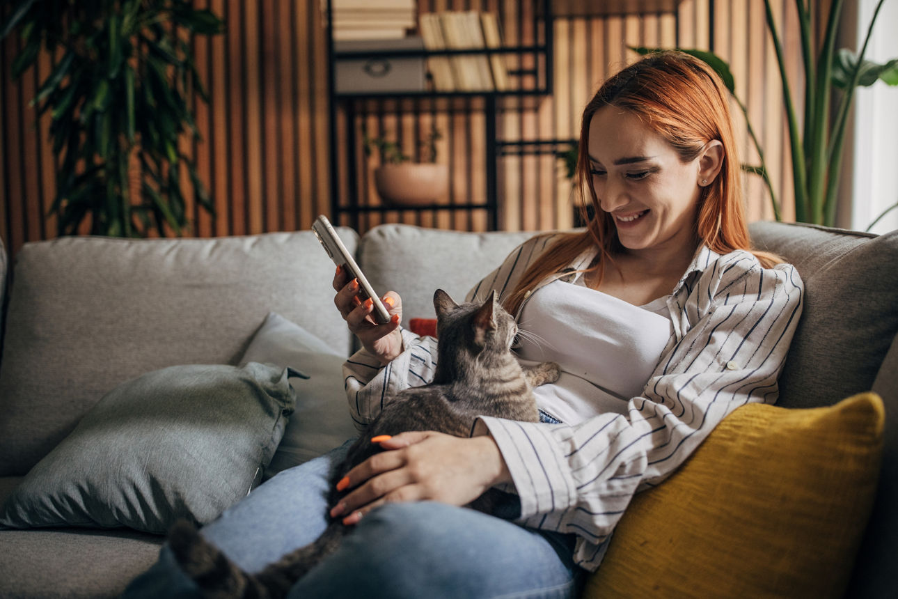 Junge Frau kuschelt mir ihrer Katze während sie ihr Smartphone benutzt