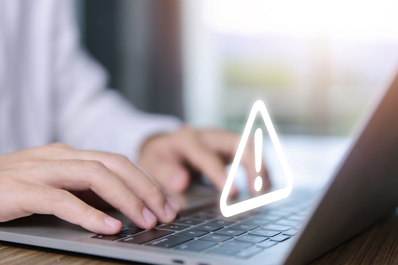 Person sitzt am Laptop und tippt - über den Fingern ist ein Warnsymbol.