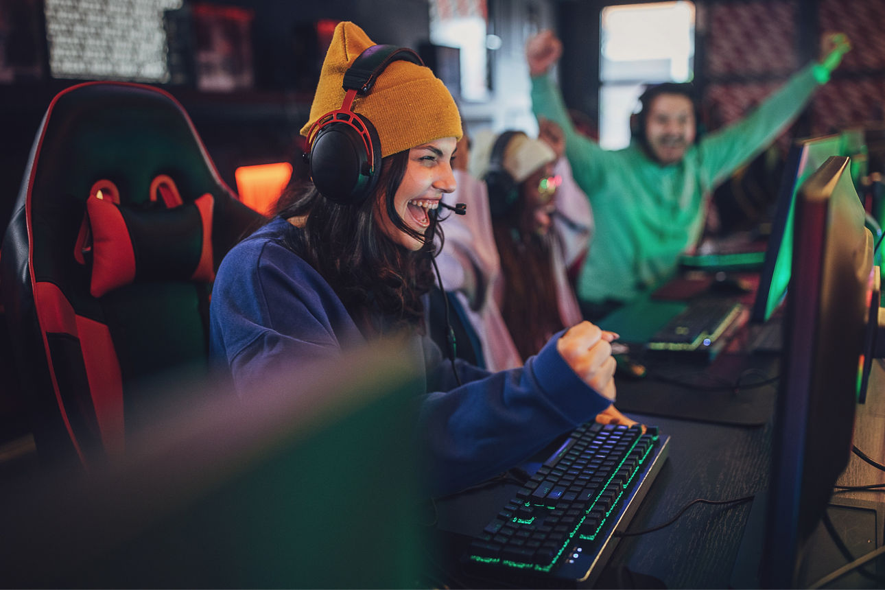 Eine Frau mit Gaming-Kopfhörer sitzt vor dem PC und freut sich