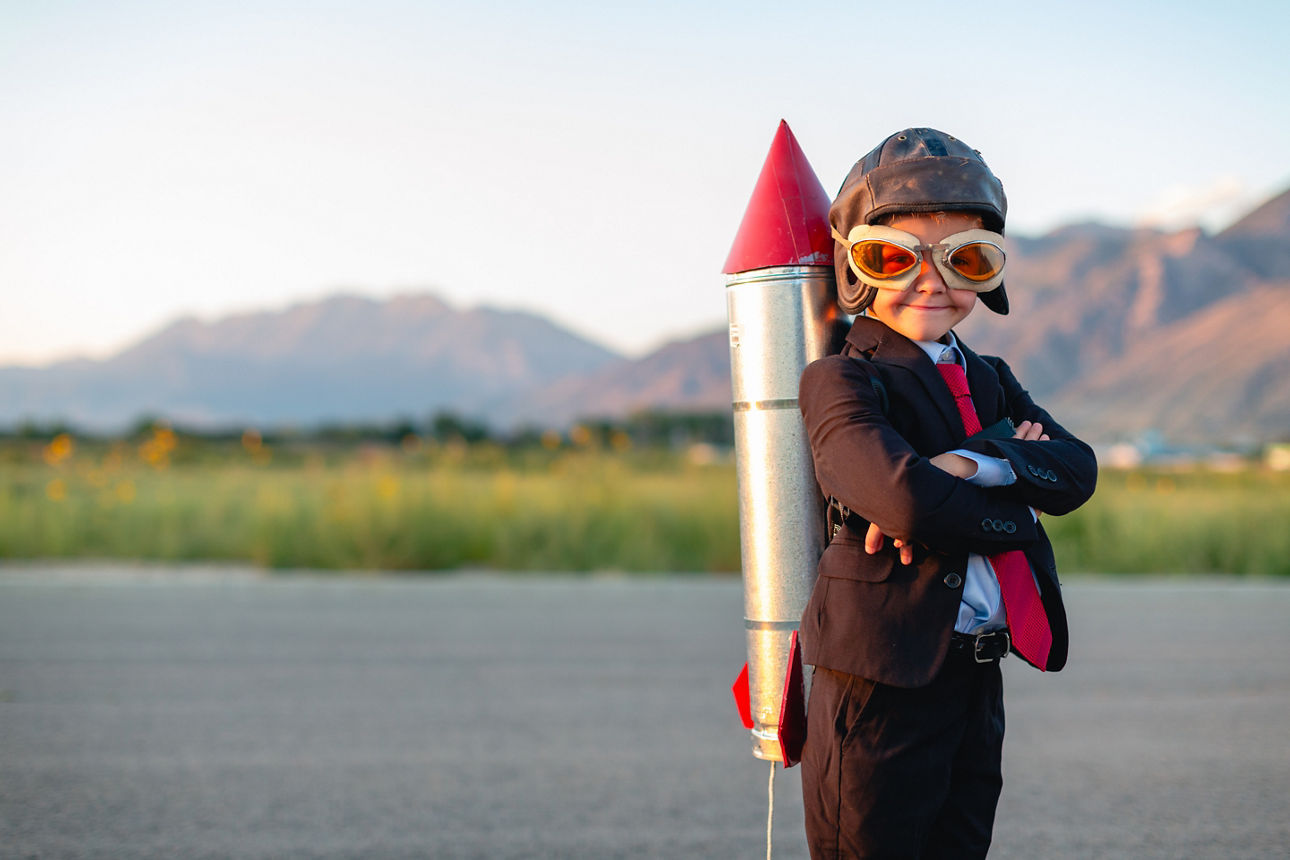 A young boy and businessman is dressed in a business suit with a homemade rocket strapped to his back. He is ready to use his smarts to launch his business to the next level. Taken in Utah, USA.
