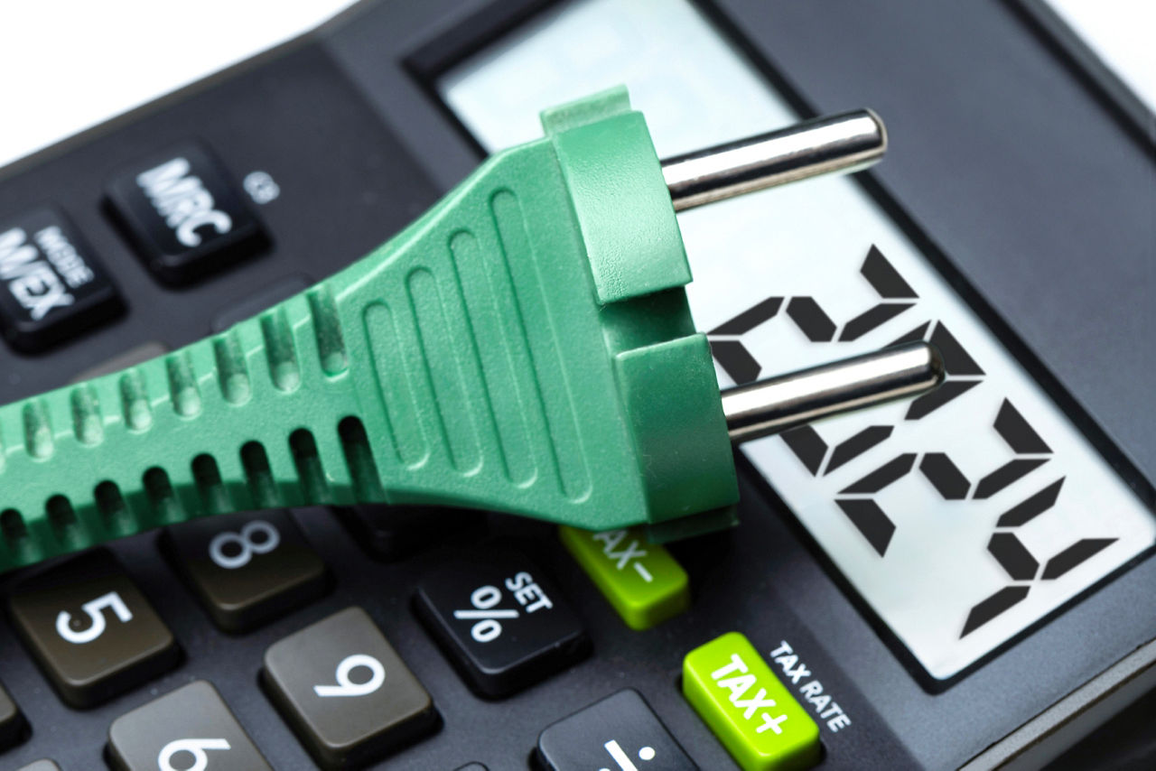 Grüner Elektrostecker mit Taschenrechner im Hintergrund symbolisiert grünen Strom