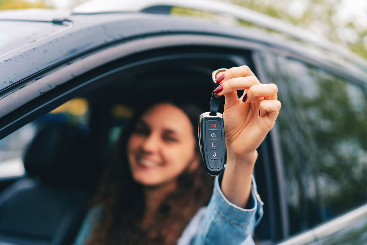 Junge Frau sitzt in ihrem Auto und zeigt stolz ihren Autoschlüssel