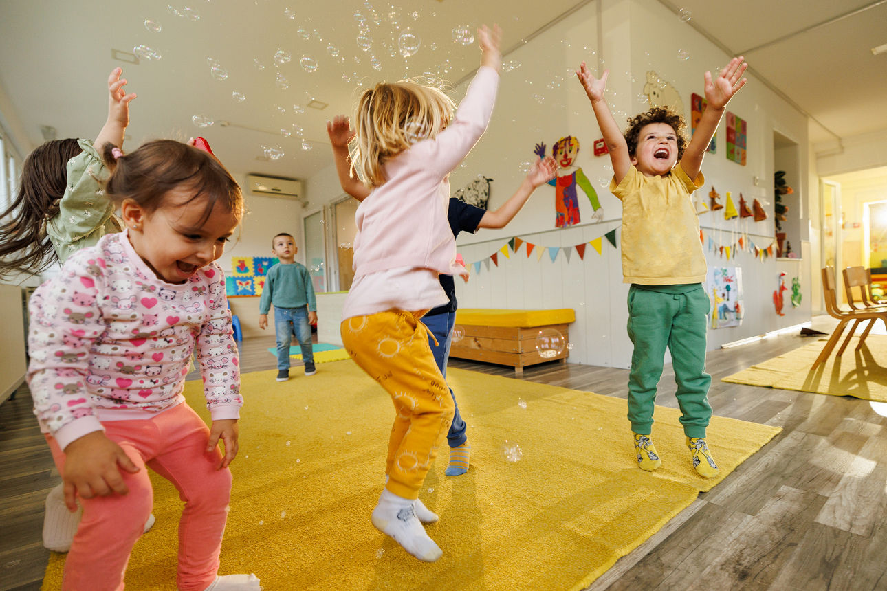 Viele Kinder springen freudig und Seifenblasen fliegen umher.