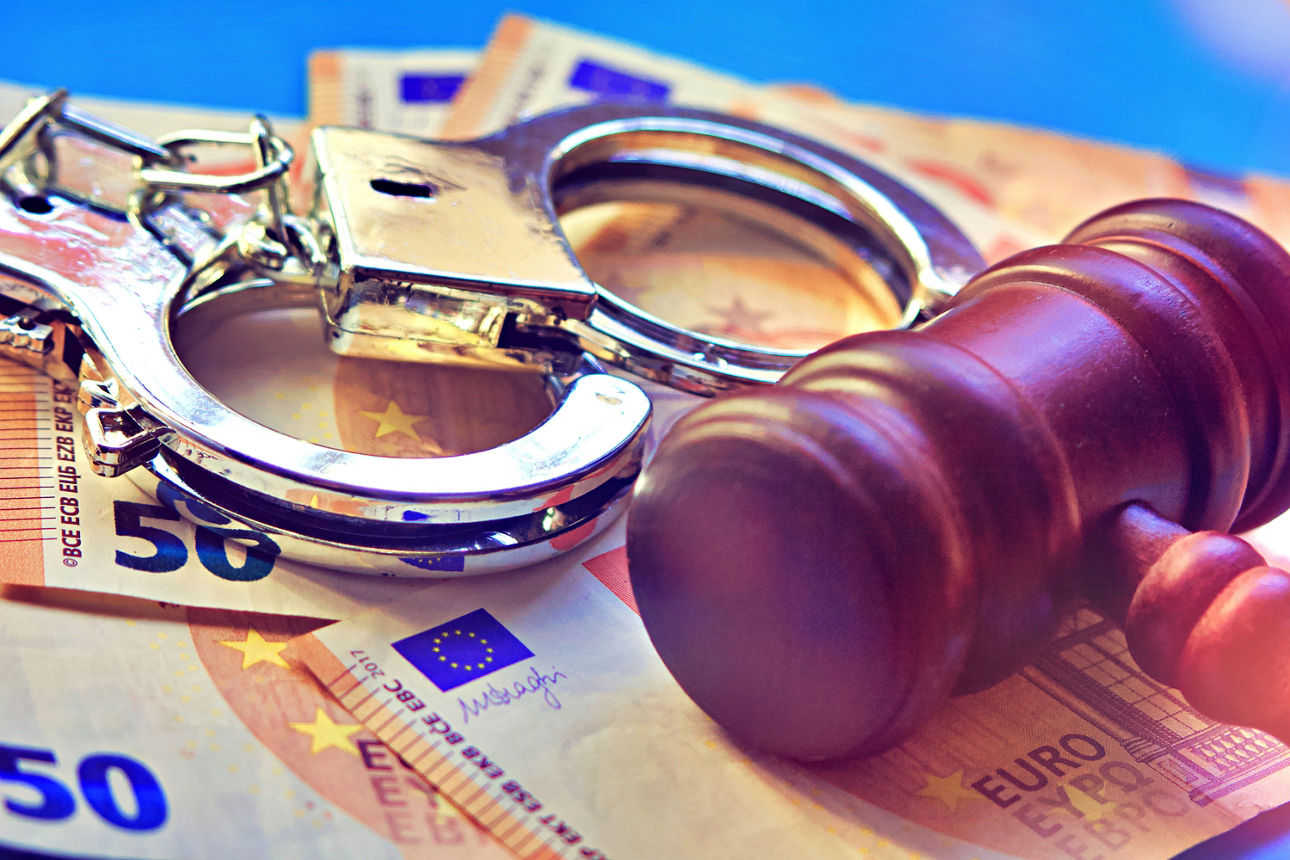 Geldscheine, auf denen Handschellen und ein Holzhammer liegen.