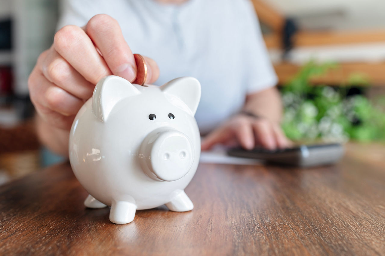 Man putting a coin into a pink piggy bank concept for savings and finance