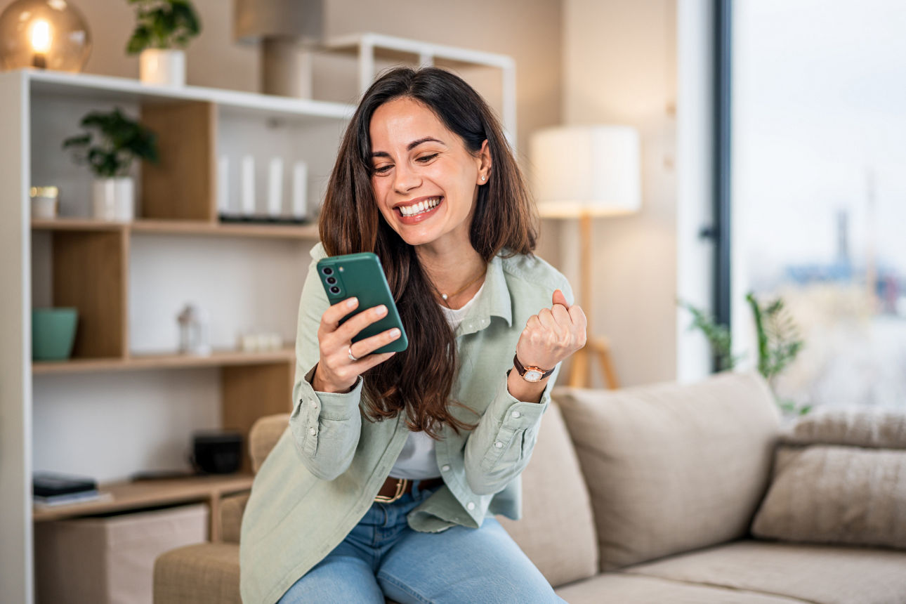 Person schaut auf ein Smartphone im Wohnzimmer und reagiert auf eine Nachricht. Das Bild symbolisiert die Freude über einen G