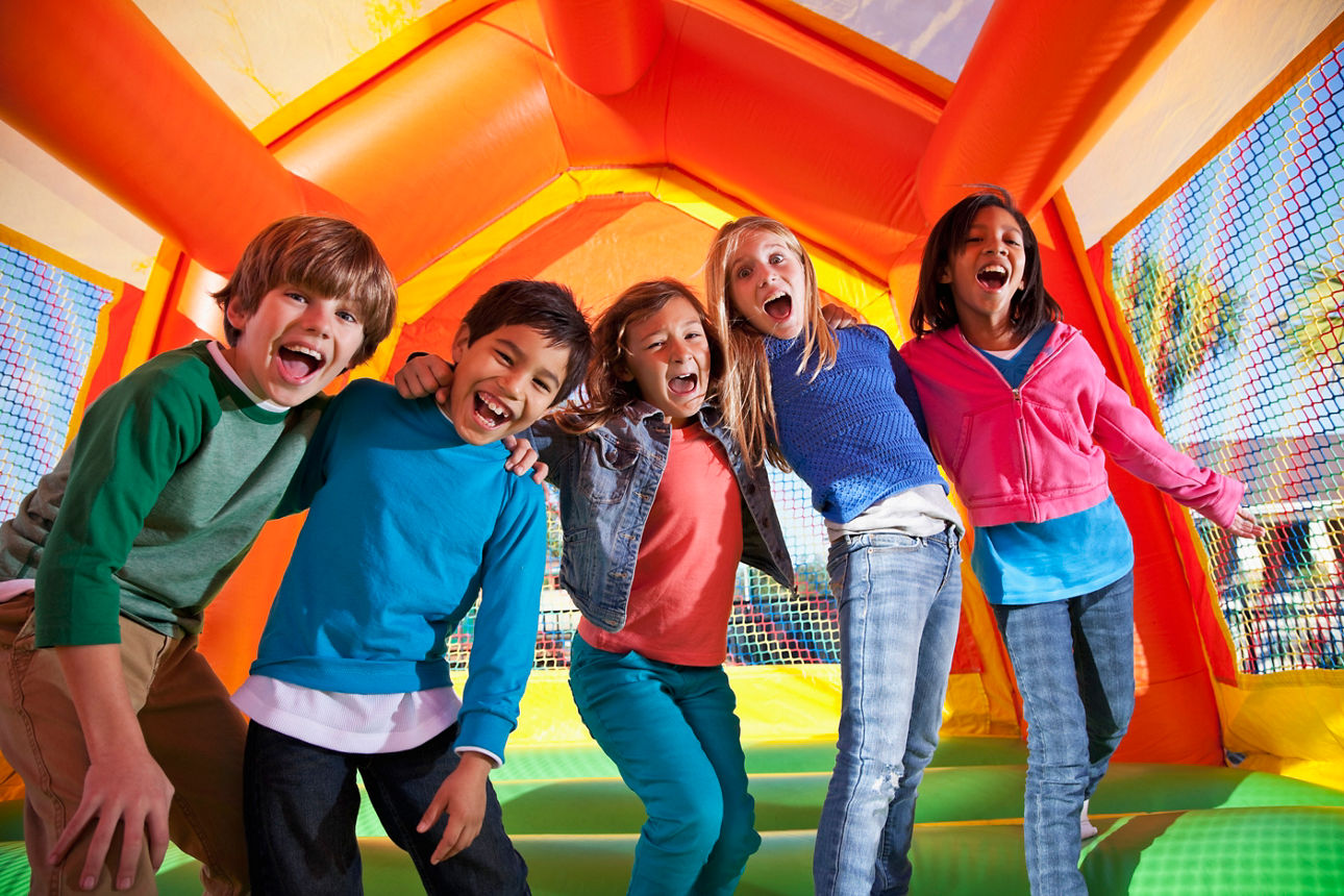 Eine Gruppe von fünf Kindern lachen und haben Spaß in einer Hüpfburg. 