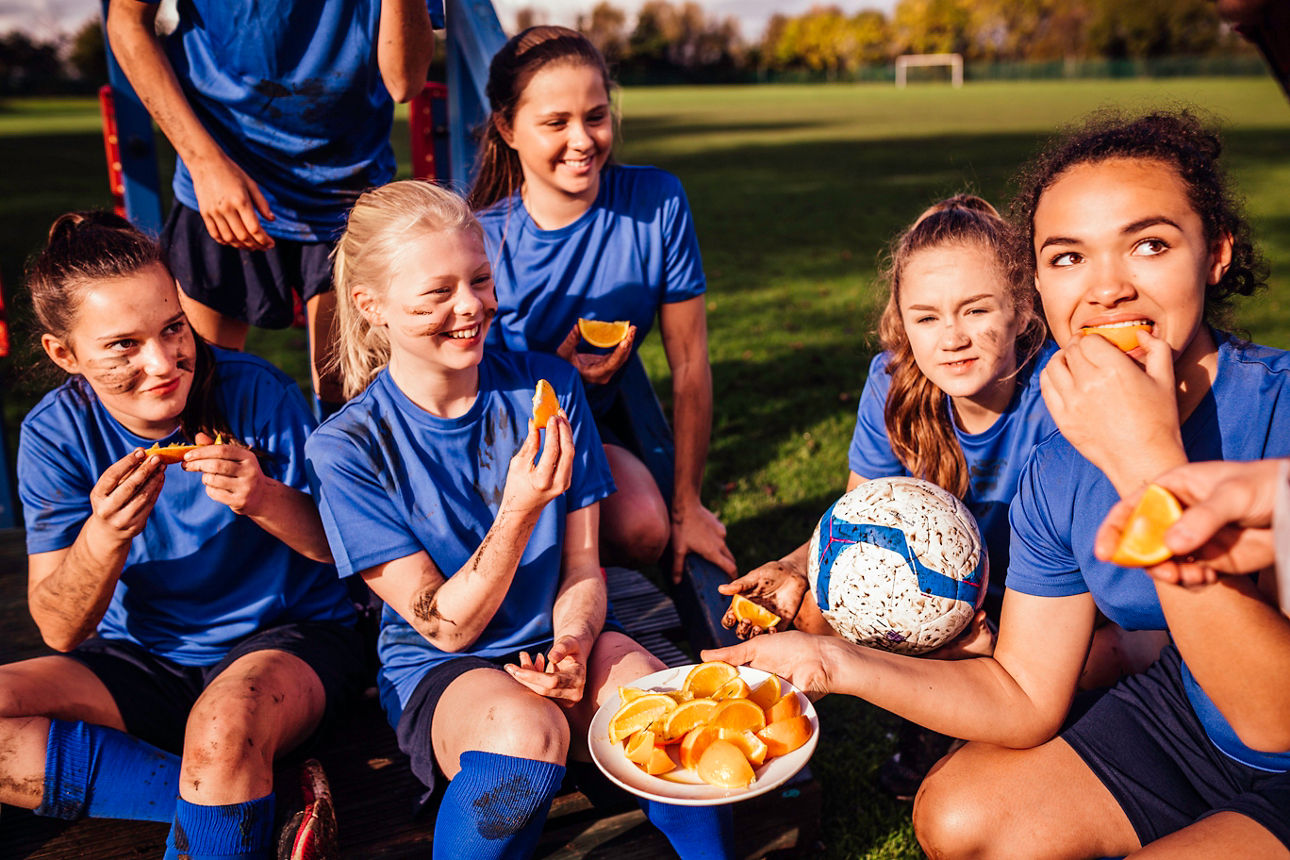 Fußballspielerinnen, die gemeinsam am Spielfeld sitzen und Orangenspalten essen