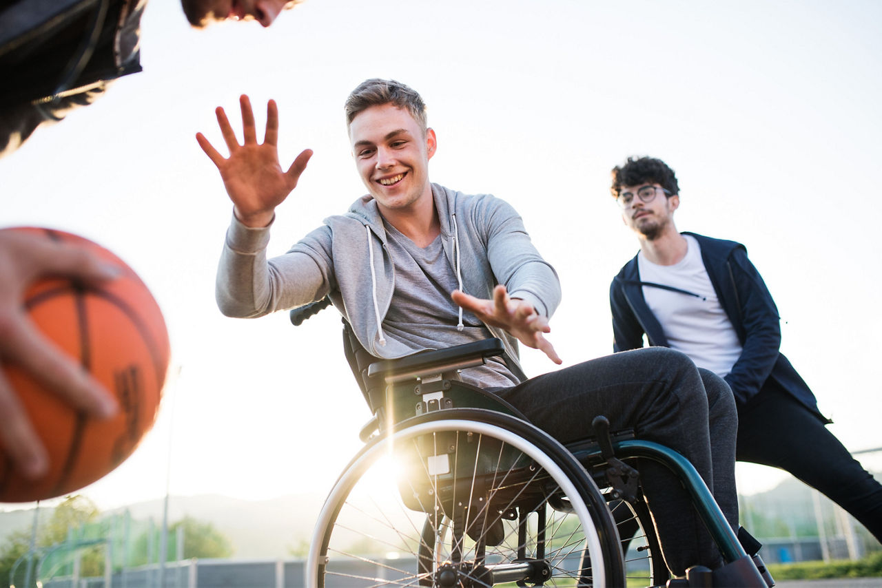 Ein junger Erwachsener im Rollstuhl spielt Basketball mit seinen Freunden