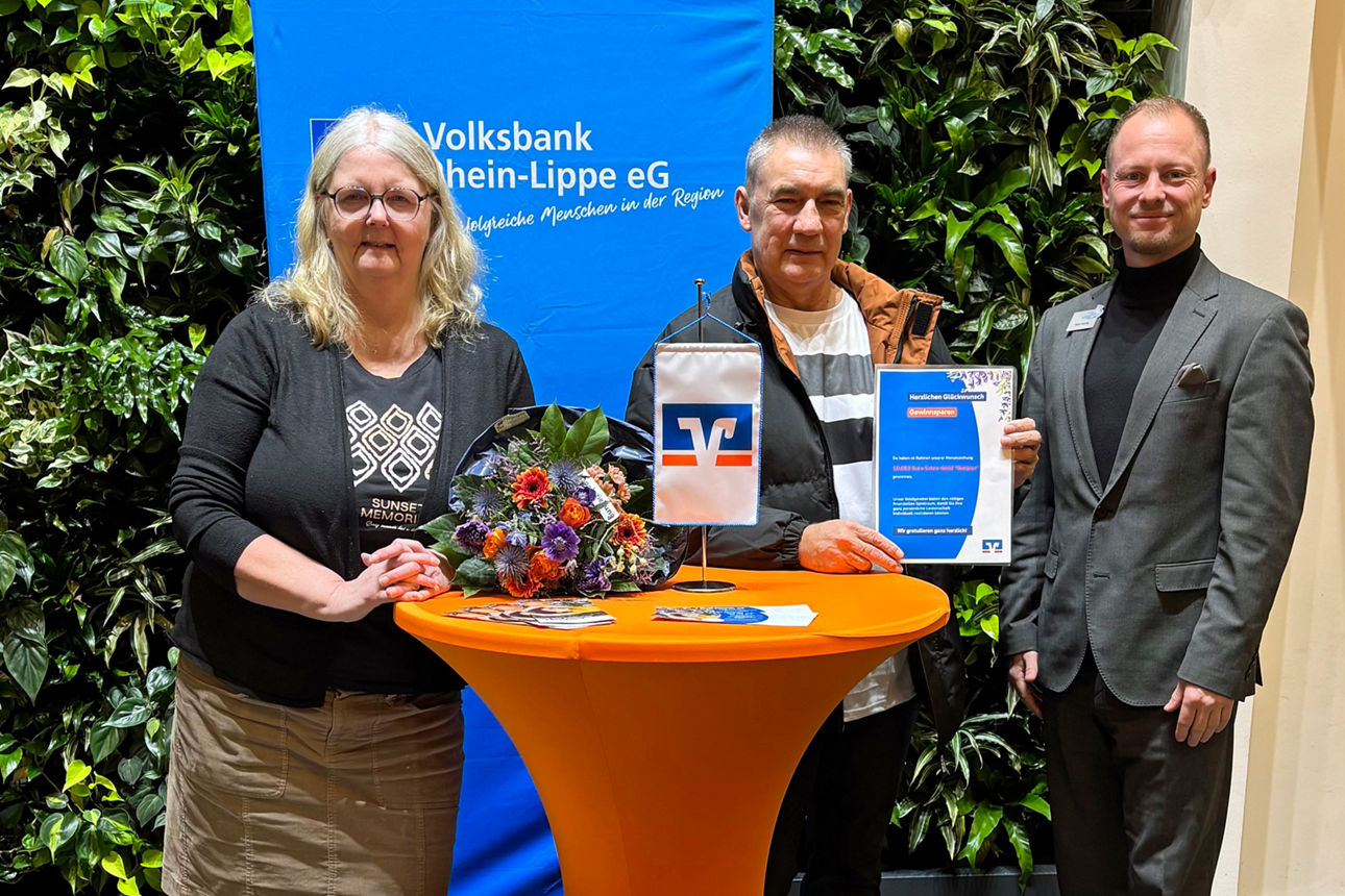 Drei Personen an einem Stehtisch vor einer Pflanzenwand. 