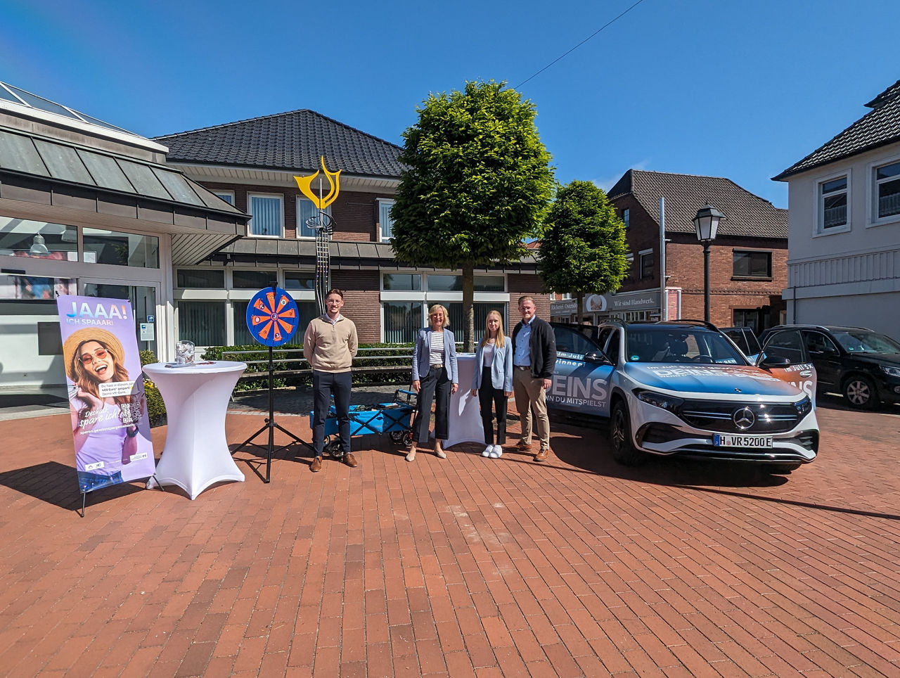 4 Personen mit einem Stand zum Thema Gewinnsparen vor der Bank