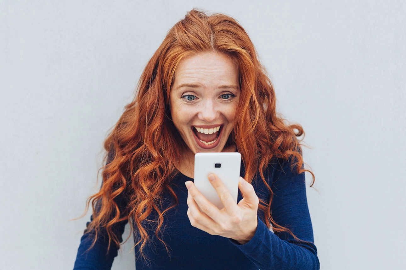 Eine junge Frau hält ein Handy und freut sich