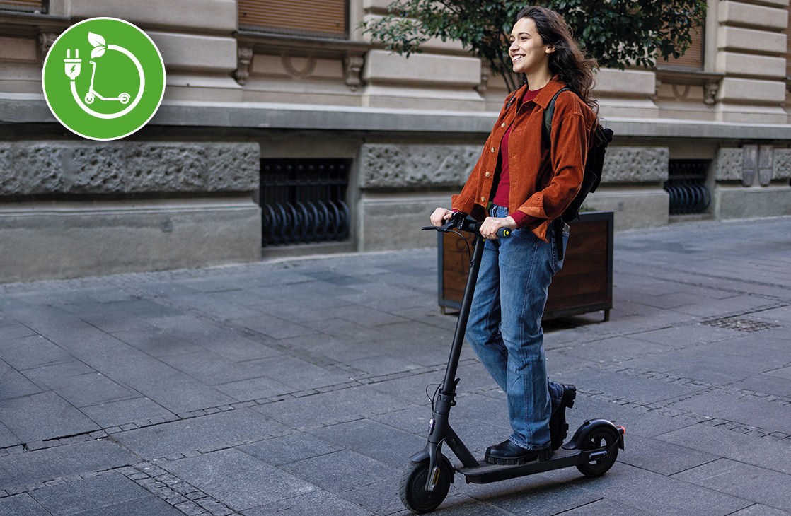 Junge Frau fährt mit einem E-Roller auf einem Gehsteig