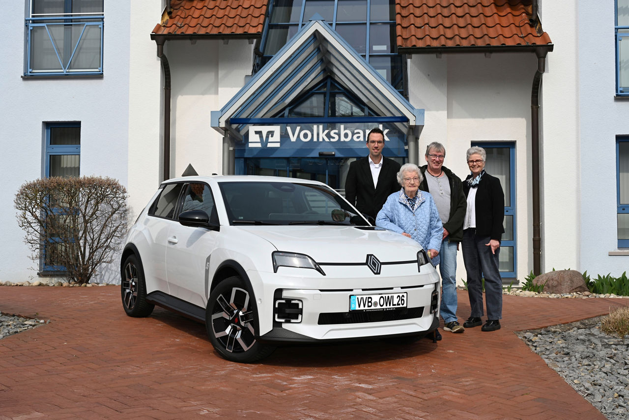 Eine Frau steht zusammen mit ihrem Sohn und zwei Mitarbeitern der Volksbank Höxter vor ihrem gewonnenen Renault 5 E-Tech. 