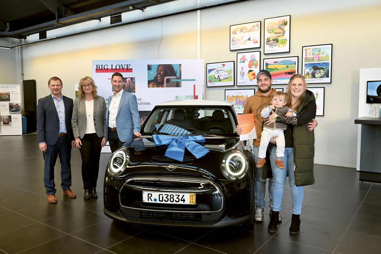 Gewinnspargewinner und Mitarbeiter*Innen bei der Übergabe des Mini Coopers
