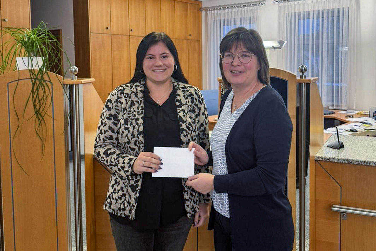 Zwei Frauen bei Scheckübergabe im Bankbüro, gemeinsames Foto im Innenraum